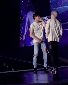 a man singing into a microphone while standing next to another man on a stage