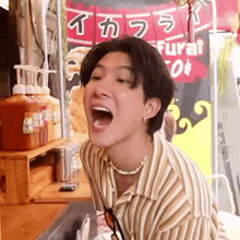 a young man is making a funny face with his mouth open in front of a food stand .