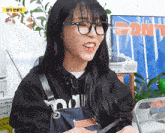 a woman wearing glasses and an apron is smiling in front of a poster that says do it