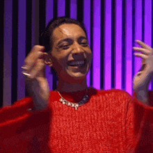 a woman wearing a red sweater and a necklace is laughing .