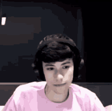 a young man wearing headphones and a pink t-shirt is sitting on a couch .