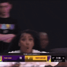a girl is sitting in the stands watching a basketball game with a scoreboard that says 11 and 7