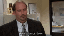 a bald man in a suit and tie is saying two thumbs down