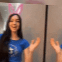 a woman wearing bunny ears and a blue shirt is standing in front of a mirror with her hands outstretched .