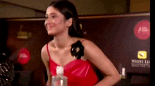 a woman in a red dress is smiling and holding a bottle of alcohol .