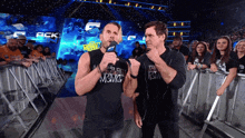 two men standing in front of a crowd with one wearing a shirt that says among
