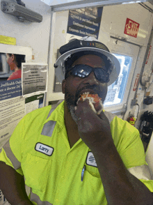 a man wearing a hard hat and sunglasses named larry is eating a piece of pizza