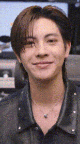a close up of a man wearing a necklace and a leather jacket .