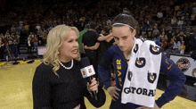 a woman with a gatorade towel on her shoulder talks to a reporter