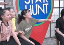 a group of young girls are sitting in front of a star hunt sign .