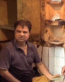 a man wearing a blue shirt that says ' reebok ' on it sits in a kitchen