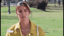 a woman in a yellow shirt is standing in a park with a scarf around her head .
