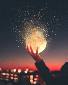 a person holding a full moon in their hand with sparkles coming out of it