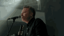 a man is singing into a microphone while holding a guitar