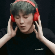 a man with green hair is wearing red headphones and making a face .