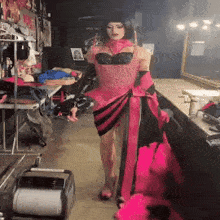 a drag queen in a pink and black dress is walking in a dressing room