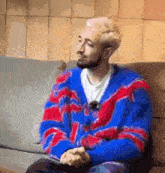 a man in a blue and red sweater is sitting on a couch .
