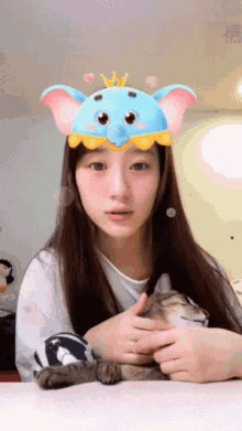 a woman wearing a blue elephant hat holds a cat