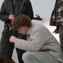 a man with curly hair is kneeling down in front of another man