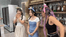 three women are standing in front of a bar with bottles of smirnoff on shelves
