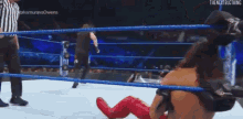 a wrestler is laying on the floor in a wrestling ring while a referee stands behind him .