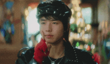 a young man wearing a black hat and red gloves holds his hand to his chin .