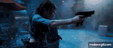 a woman in a blue shirt is holding a gun in a dark room ..