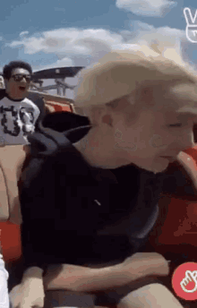 a man with blonde hair is riding a roller coaster with a peace sign in the foreground