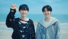 two young men standing on a beach with one wearing a black sweater