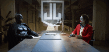 batman and the joker are sitting at a table with a jl logo behind them
