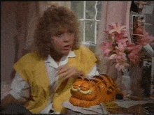 a woman in a yellow vest sits at a desk with a garfield statue