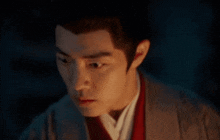 a close up of a man 's face in a dark room . he is wearing a kimono and a red vest .