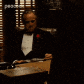 a man in a tuxedo sits at a desk and says don corleone give me justice