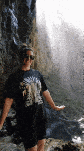 a woman standing in front of a waterfall wearing a black space spice shirt