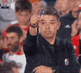 a man in a suit is giving a thumbs up sign while sitting in the stands .