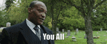 a man in a suit and tie is standing in a cemetery saying you all .