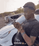 a man is standing in front of a white car holding a cell phone .