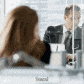 a man in a suit and tie is talking to a woman who is sitting at a desk with a laptop and says donna