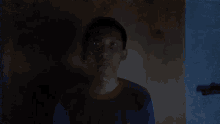 a young man in a blue shirt stands in the dark