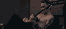 a shirtless man is holding a guitar and pointing at something .