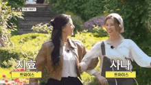 two women are standing next to each other in a park holding hands .
