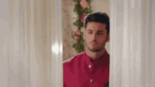a man in a red shirt is peeking out of a doorway