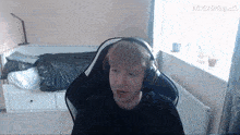 a man wearing headphones sits in front of a bed with pixverse.ai written on the bottom right