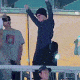 a man in a blue shirt and black hat is standing in front of a crowd with his arms in the air .