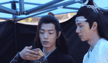 two men are standing next to each other and one is looking at his phone .