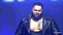 a man with a beard is wearing a leather jacket and standing in front of a blue background .