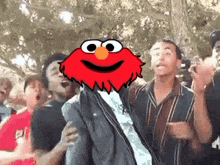 a group of people are standing around a tree with elmo 's head on their heads .