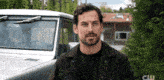 a man with a beard is standing in front of a car that has the letters cw on it