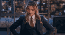 a woman in a suit and tie is standing with her hands on her hips and looking at the camera .