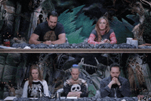 a group of people sitting at a table with one wearing a skull shirt
